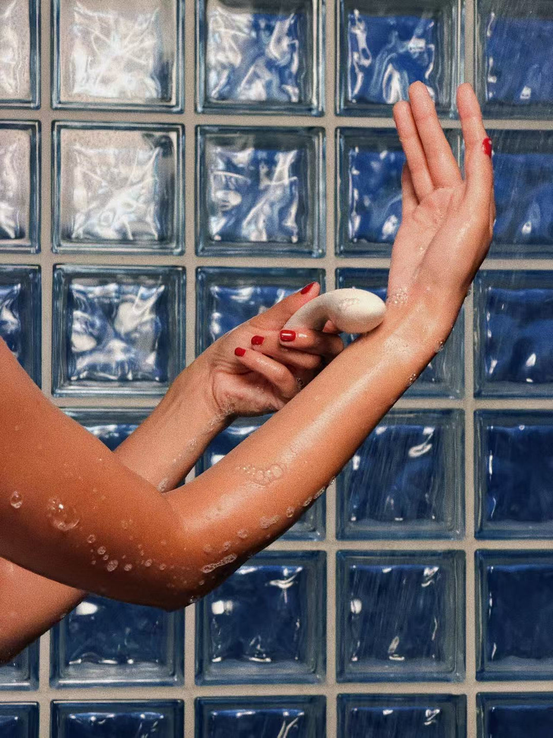 Hands holding The Stir, a slim curved G-spot vibrator, under the shower